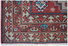 A vintage handwoven Caucasian wool rug featuring geometric patterns in red, blue, and beige.