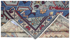 A vintage handwoven Caucasian wool rug featuring geometric patterns in blue, red, and beige.