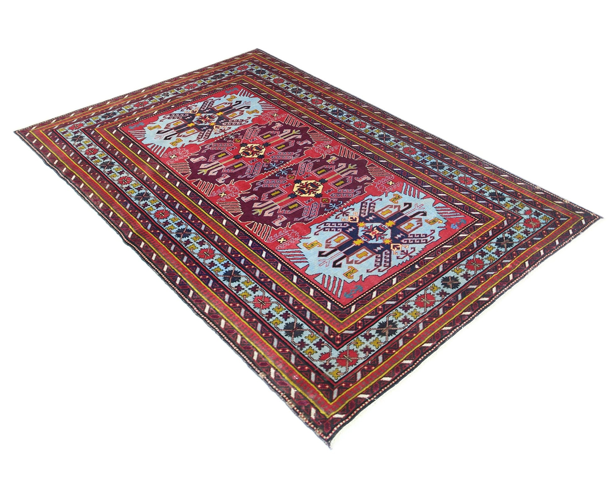 A vintage Caucasian rug featuring geometric patterns in red, blue, and yellow on a wool pile.