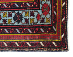 A close-up of a vintage Caucasian rug featuring geometric patterns in red, blue, and yellow.