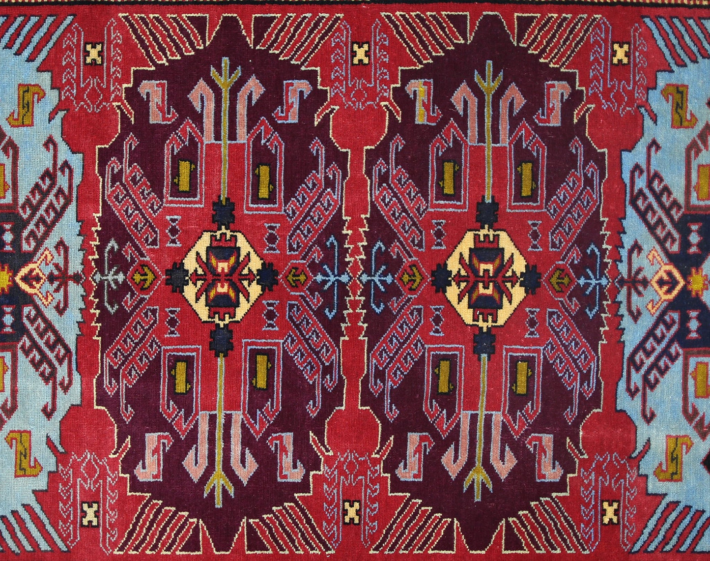 A vintage Caucasian rug featuring a symmetrical geometric pattern in deep red, blue, and yellow.