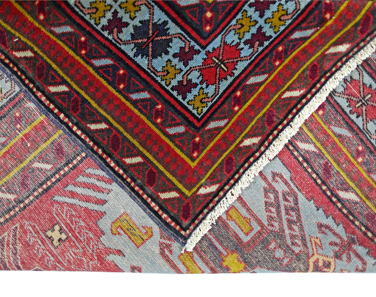 A vintage handmade Caucasian rug featuring intricate geometric patterns in red, blue, and yellow.