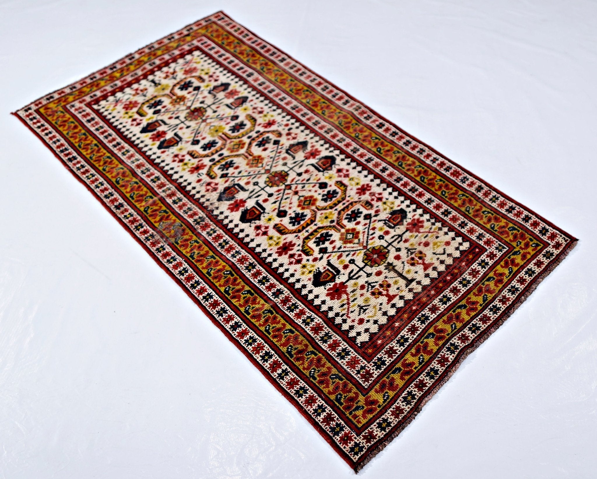 A rectangular vintage Caucasian rug featuring intricate geometric patterns in red, gold, and cream.