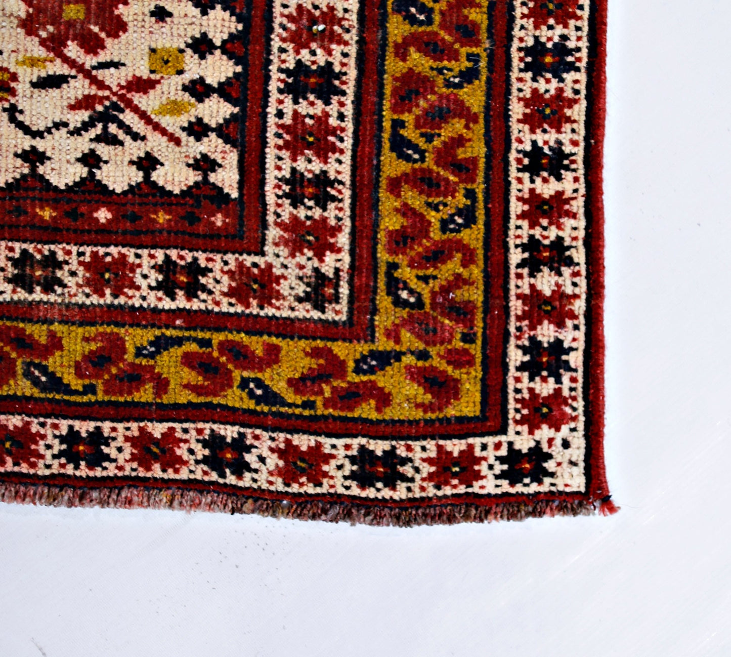 A vintage handmade Caucasian rug featuring a geometric pattern in red, yellow, and cream tones.