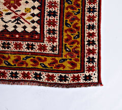 A vintage handmade Caucasian rug featuring a geometric pattern in red, yellow, and cream tones.