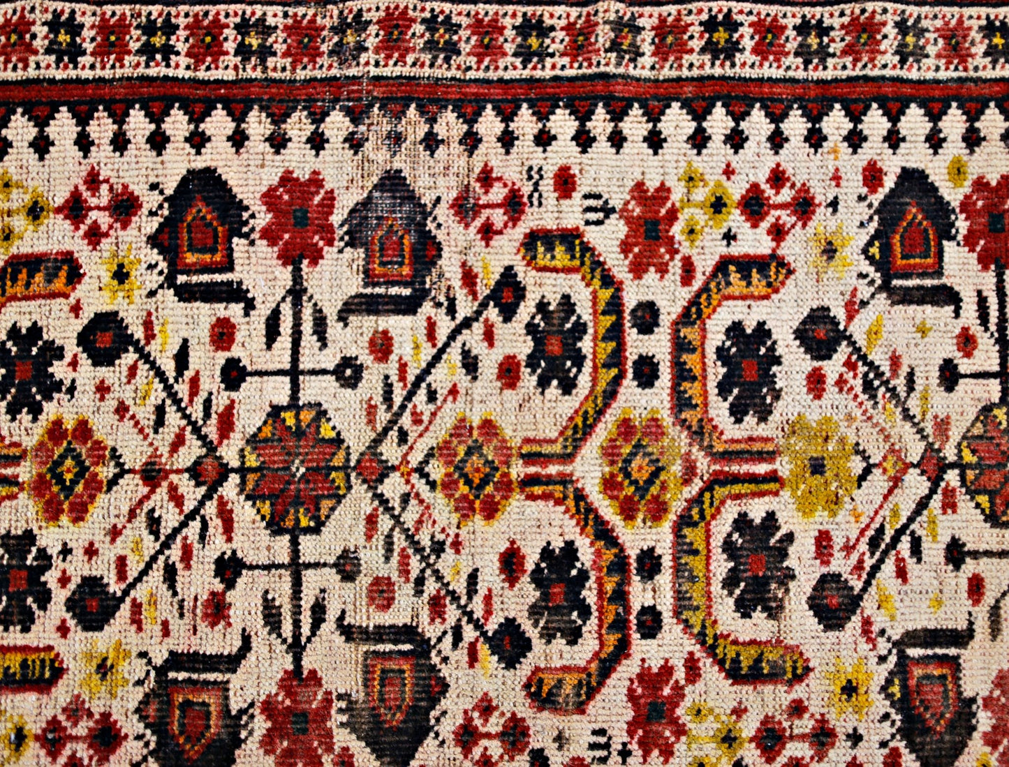 A vintage Caucasian rug featuring a geometric pattern in red, yellow, and black on a cream base.