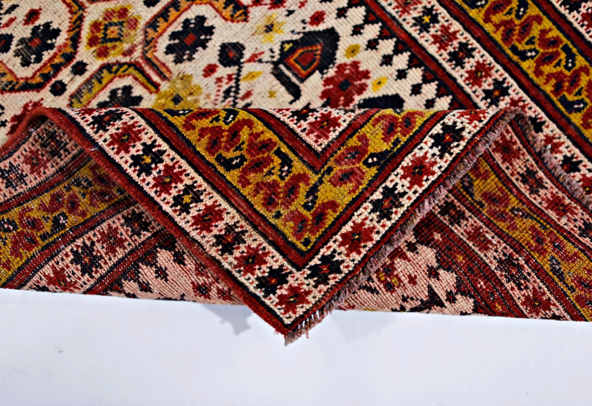 A vintage Caucasian rug with a folded corner revealing intricate geometric patterns in red and gold.