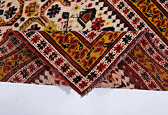 A vintage Caucasian rug with a folded corner revealing intricate geometric patterns in red and gold.