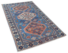 A handwoven vintage Caucasian rug featuring geometric patterns in blue, orange, and cream.