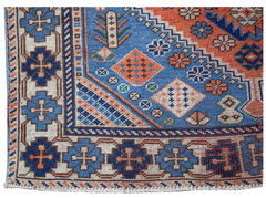 A vintage handwoven Caucasian rug featuring geometric patterns in blue, orange, and cream tones.