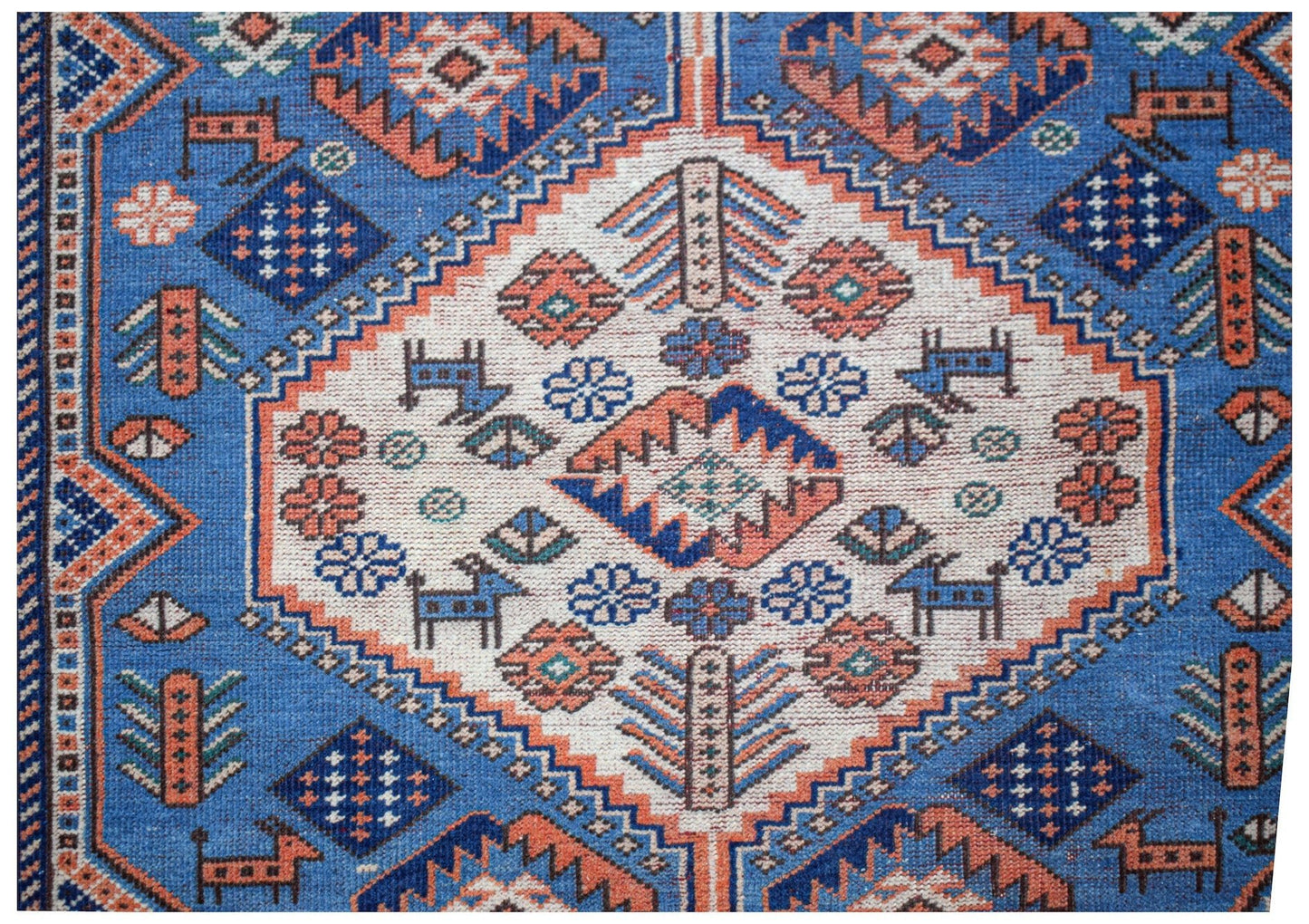 A handwoven vintage Caucasian rug featuring a blue field with geometric floral and animal motifs.