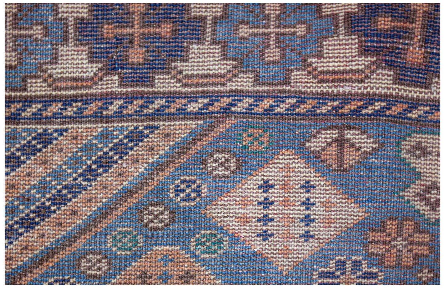 A close-up of a vintage handwoven Caucasian rug featuring geometric patterns in blue and tan.