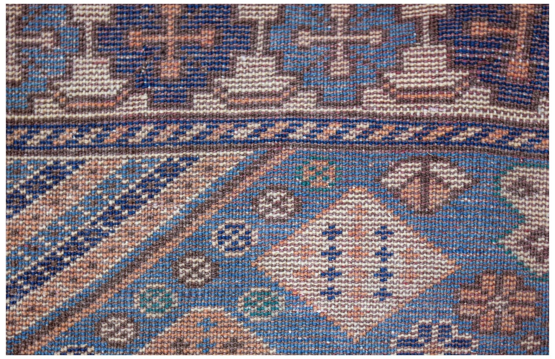 A close-up of a vintage handwoven Caucasian rug featuring geometric patterns in blue and tan.