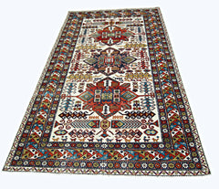A handwoven vintage Caucasian rug featuring geometric patterns in red, blue, and cream tones.