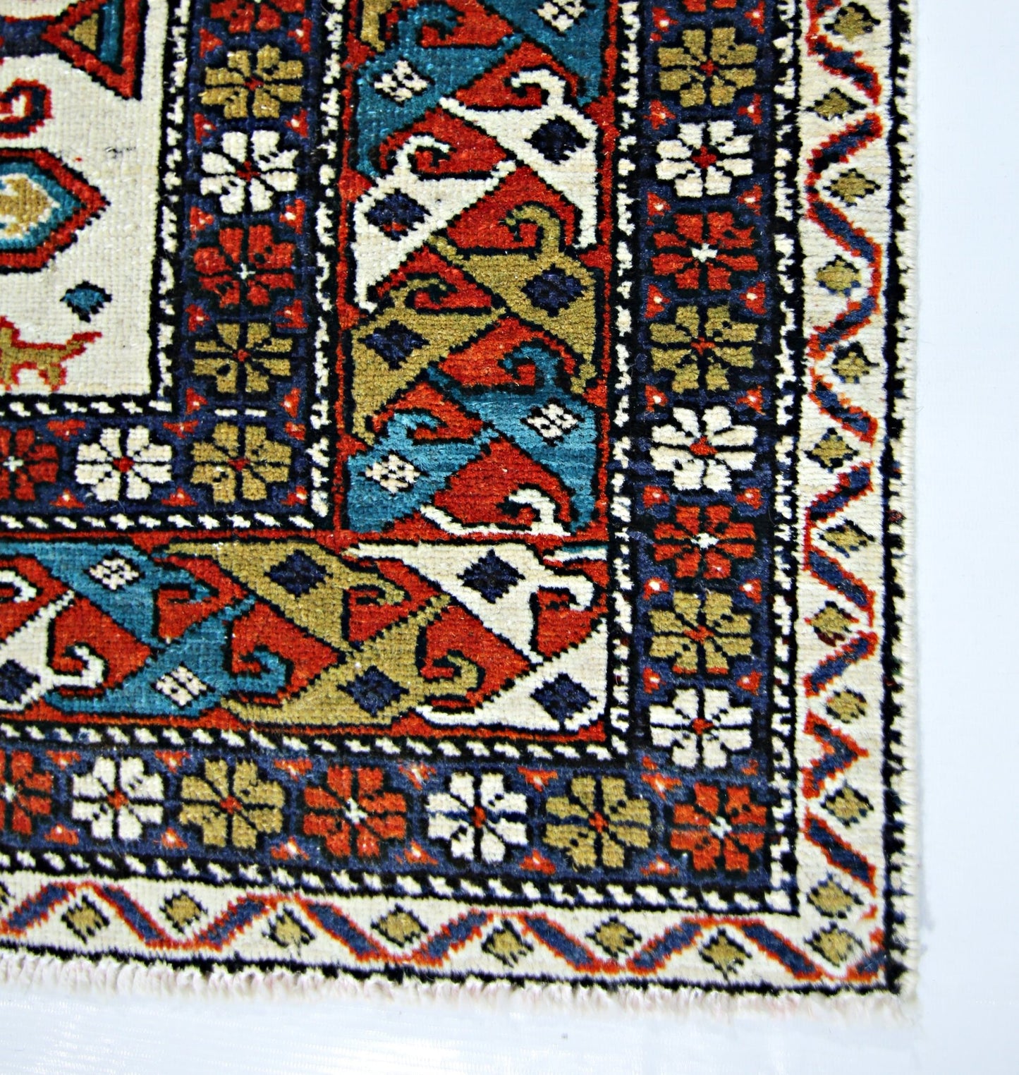 A vintage handwoven Caucasian rug featuring geometric patterns in red, blue, and gold.