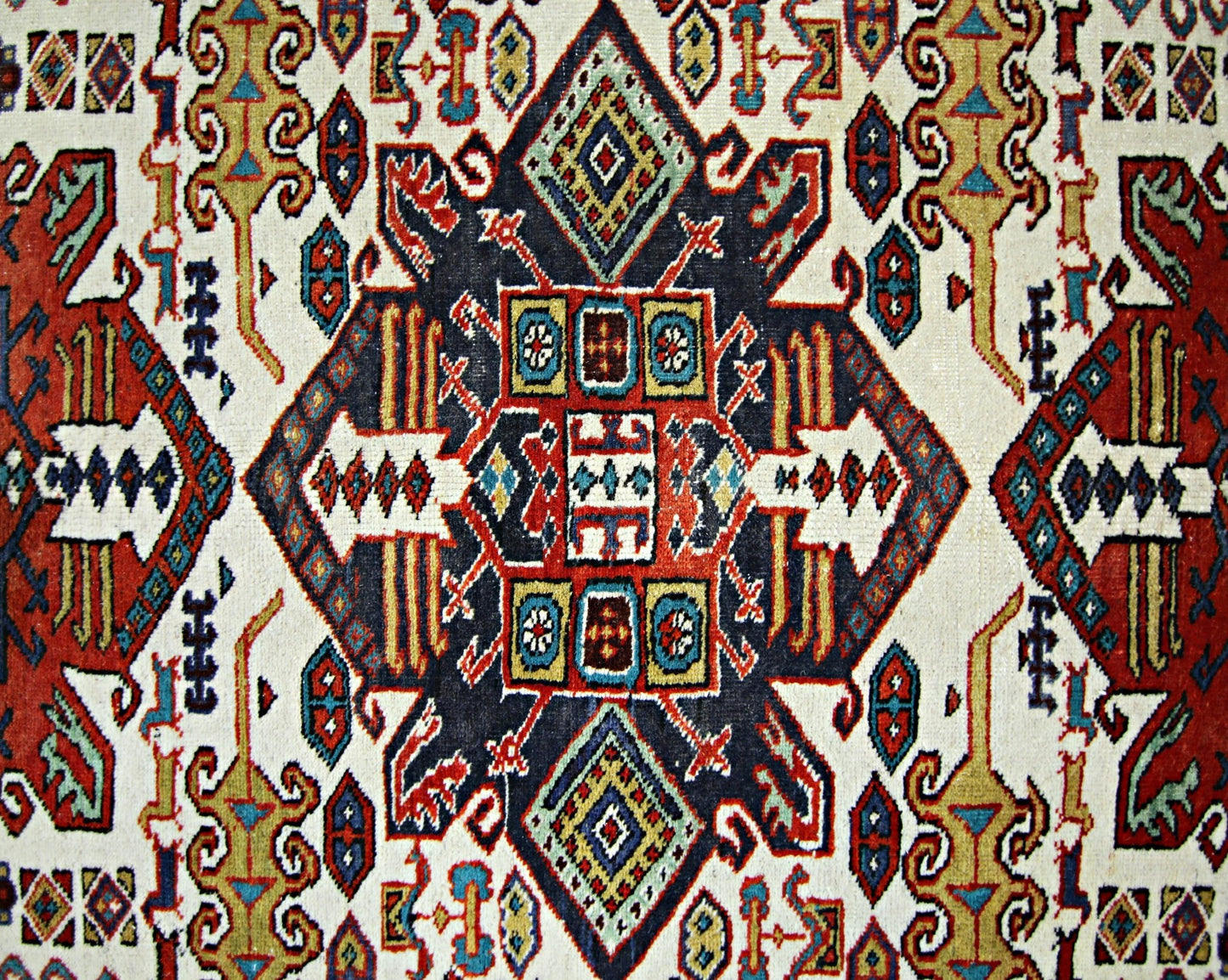 A vintage handwoven Caucasian rug featuring a geometric pattern in red, blue, and cream tones.