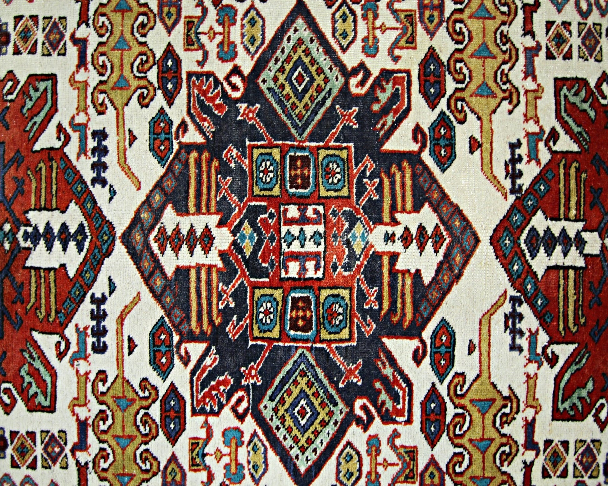 A vintage handwoven Caucasian rug featuring a geometric pattern in red, blue, and cream tones.