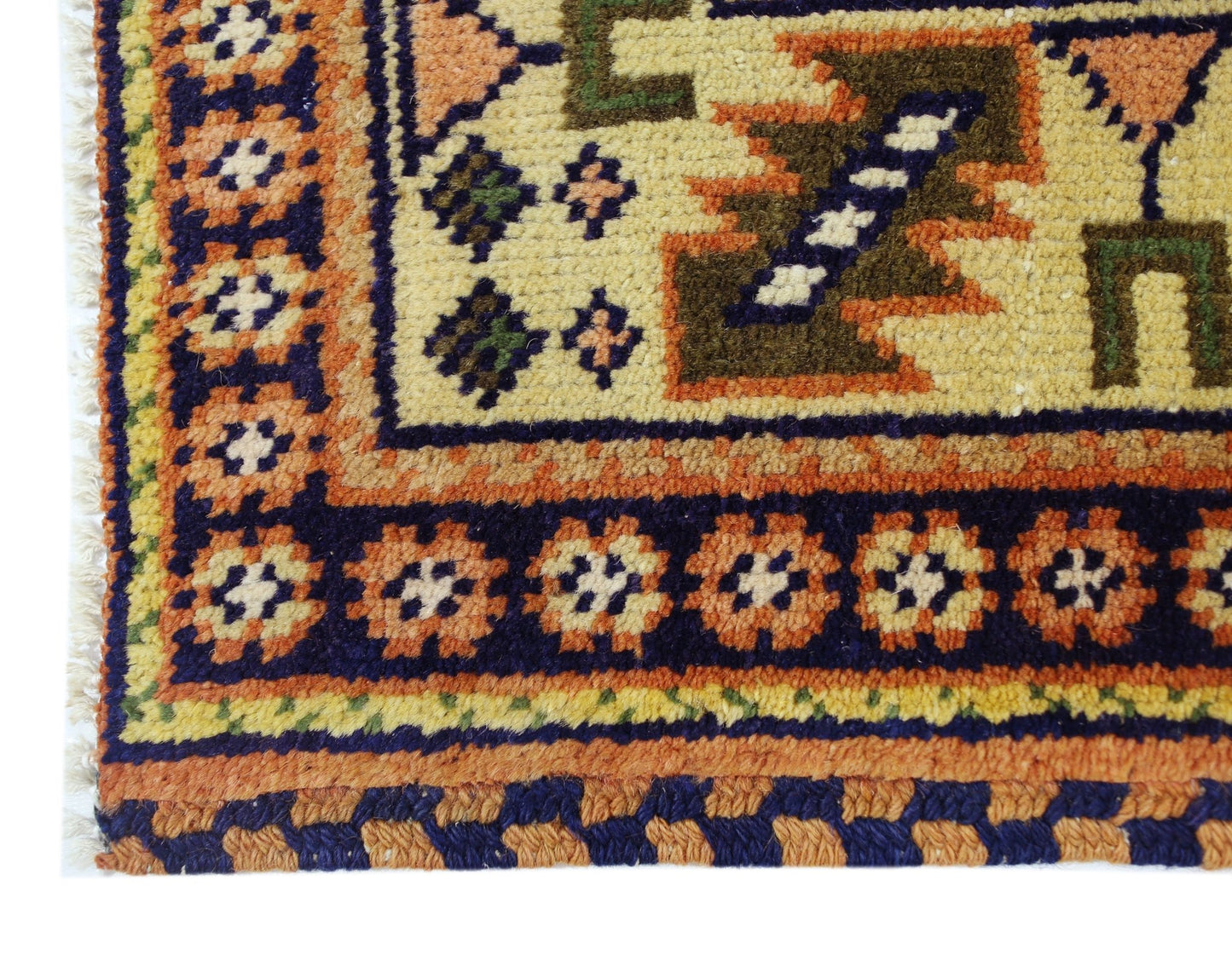 A corner view of a vintage Caucasian rug featuring geometric patterns in orange, blue, and cream.