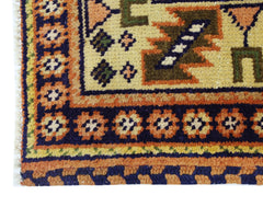 A corner view of a vintage Caucasian rug featuring geometric patterns in orange, blue, and cream.