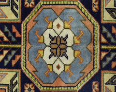 A vintage Caucasian rug featuring a central geometric floral medallion in blue, cream, and orange.