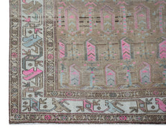 A vintage handwoven Persian rug featuring geometric patterns in brown, pink, and blue tones.