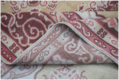 A vintage handwoven Chinese Khotan rug featuring a pink and cream floral pattern on a wool pile.