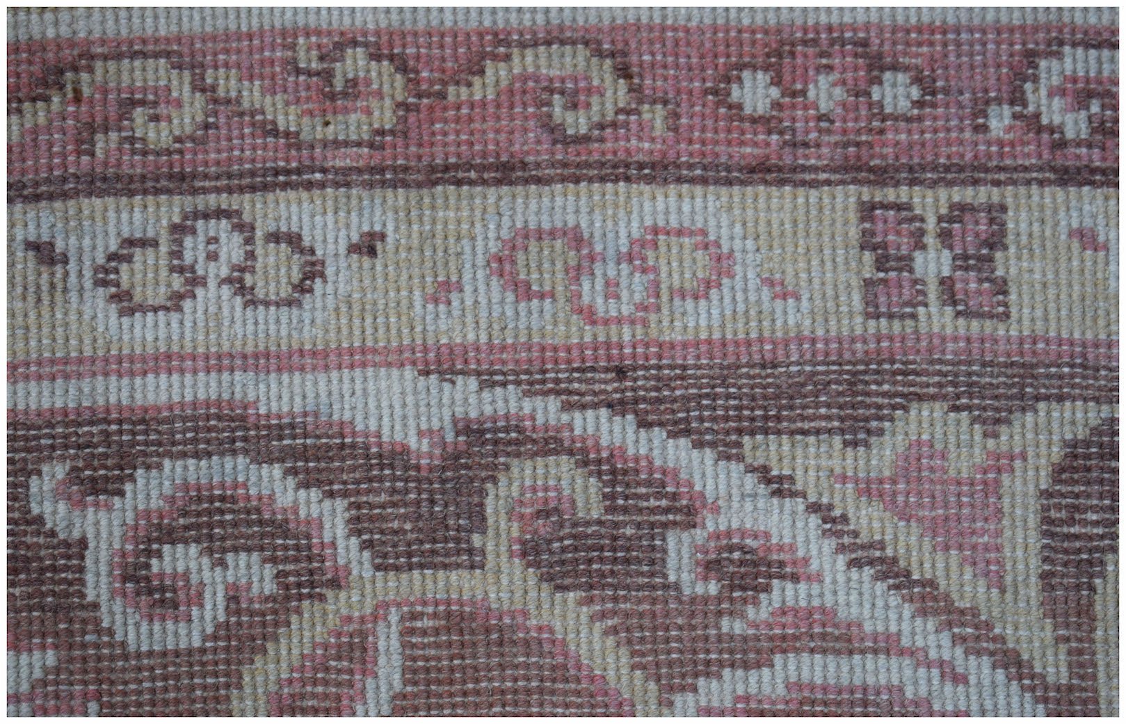 A close-up of a vintage Chinese Khotan rug featuring intricate floral patterns in pink and brown.