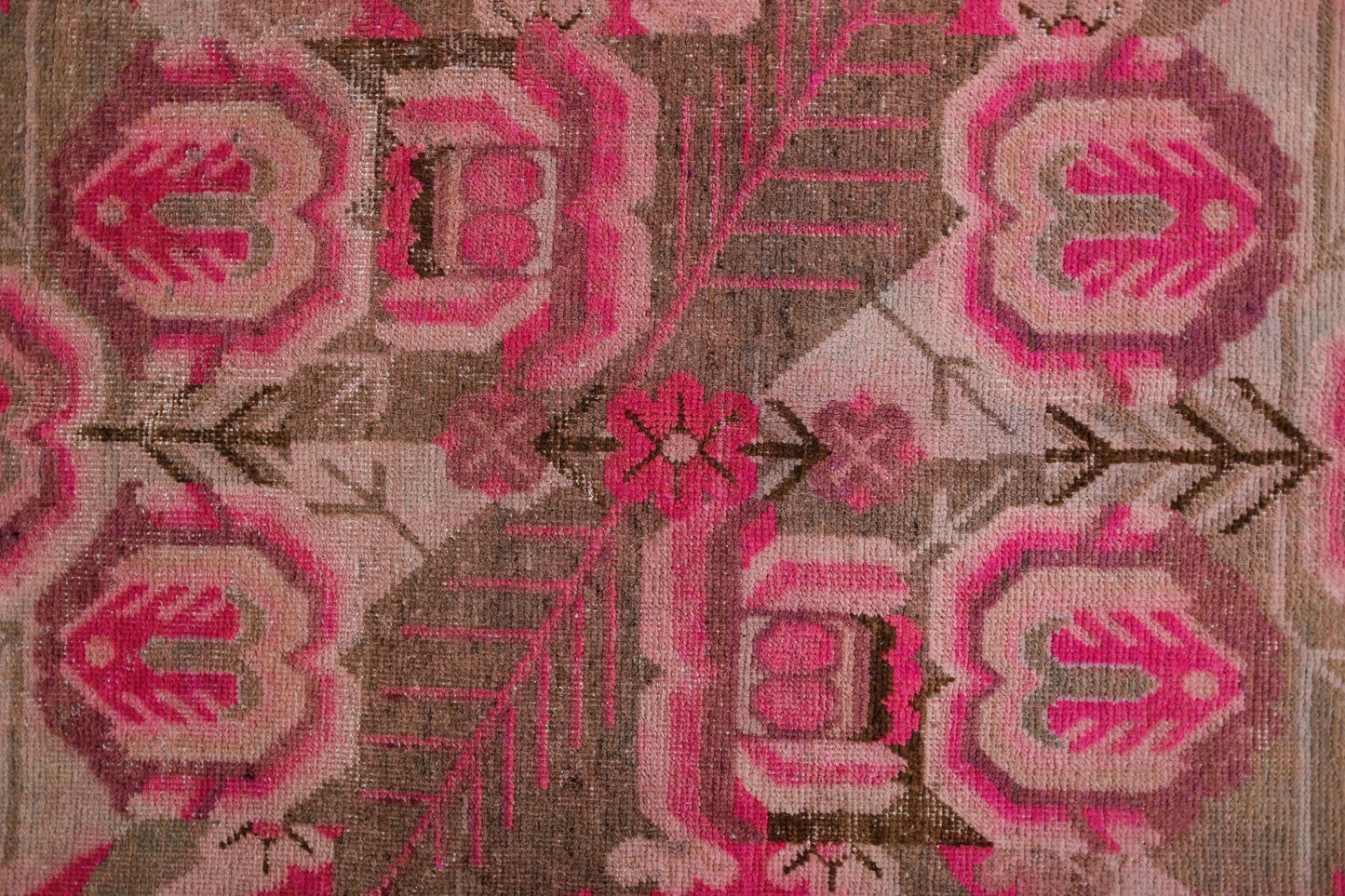 A vintage handwoven Khotan rug featuring an intricate pomegranate pattern in vibrant pink and brown.