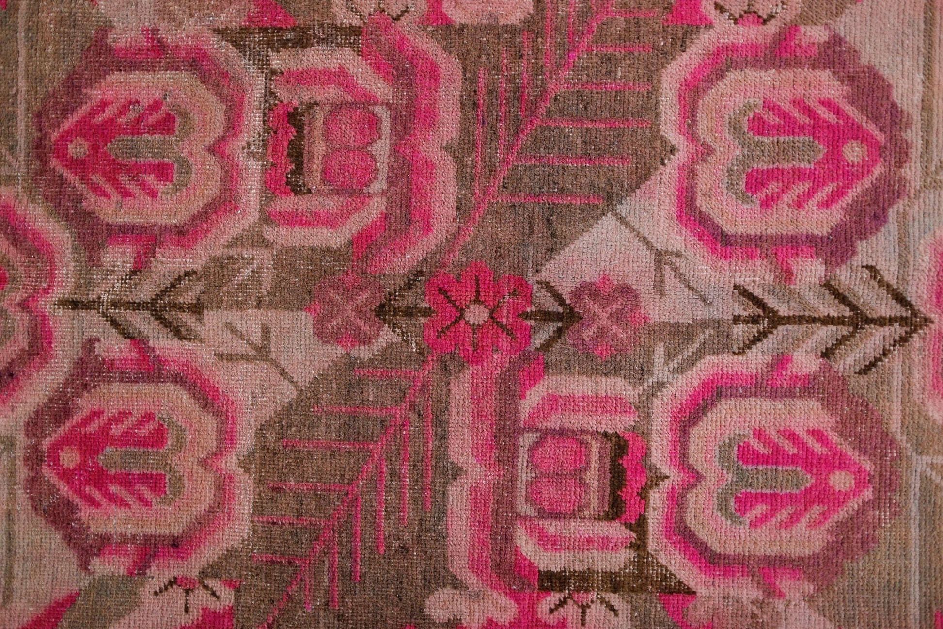 A vintage handwoven Khotan rug featuring an intricate pomegranate pattern in vibrant pink and brown.