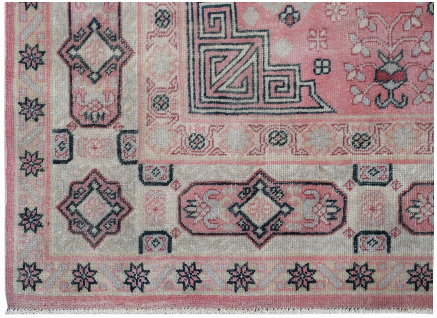 A vintage handwoven Chinese rug featuring geometric patterns in shades of pink and grey.