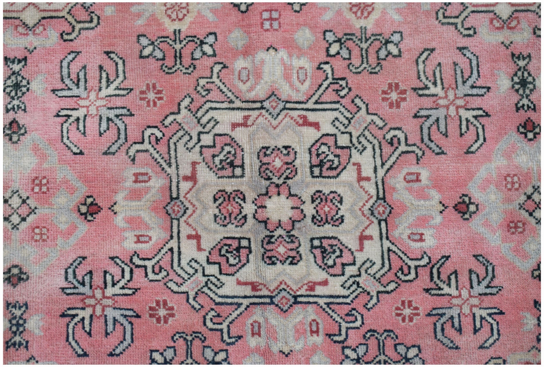 A vintage handwoven Chinese rug featuring a central floral medallion on a faded pink background.