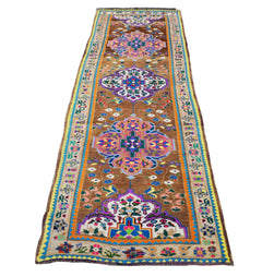 A vintage Kurdish Herki runner featuring colorful tribal motifs on a brown wool background.