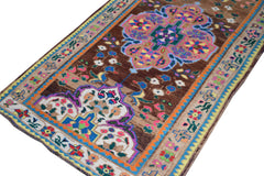 A vintage handmade Kurdish Herki runner featuring a brown field with colorful tribal motifs.