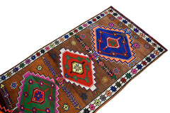 A vintage Kurdish Herki runner featuring colorful tribal geometric motifs on a brown wool field.