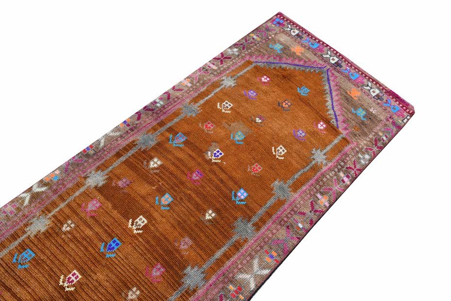A vintage Kurdish Herki runner featuring a brown field with tribal motifs and neon accents.