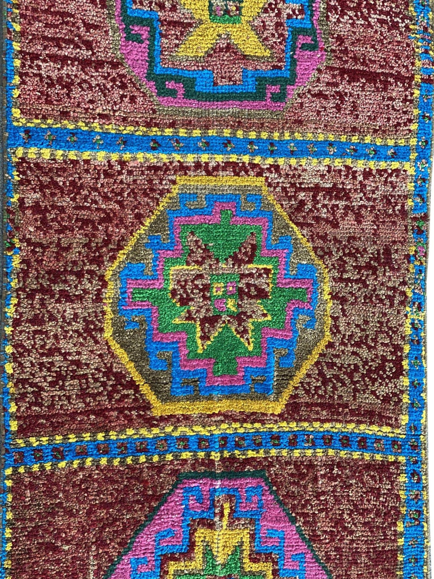 A vintage Kurdish Herki runner featuring geometric medallions in vibrant colors on a red field.