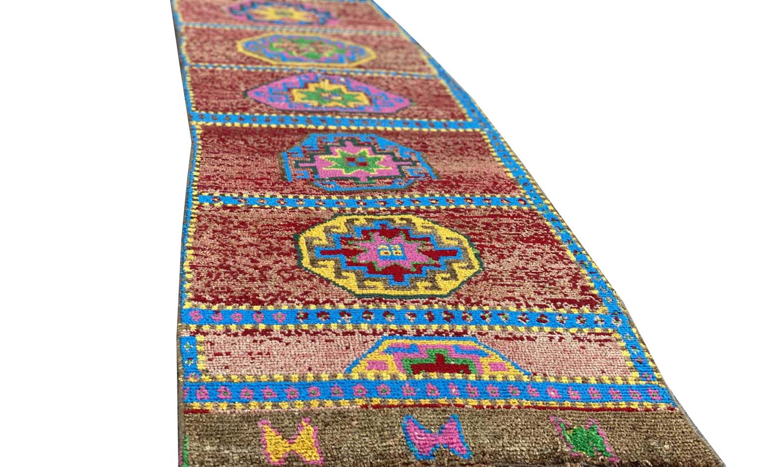 A vintage Kurdish Herki runner featuring geometric medallions in vibrant colors on a red field.