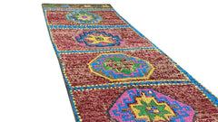 A vintage handmade Kurdish Herki runner featuring colorful geometric medallions on a red field.