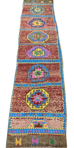 A vintage handmade Kurdish Herki runner featuring geometric medallions on a red wool background.