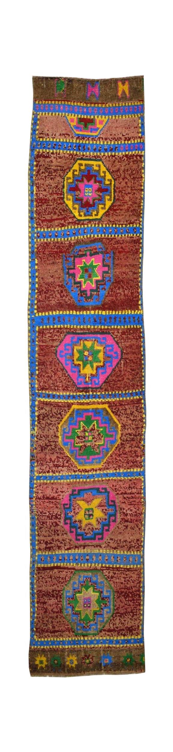 A vintage Kurdish Herki runner featuring geometric medallions on a reddish-brown wool field.