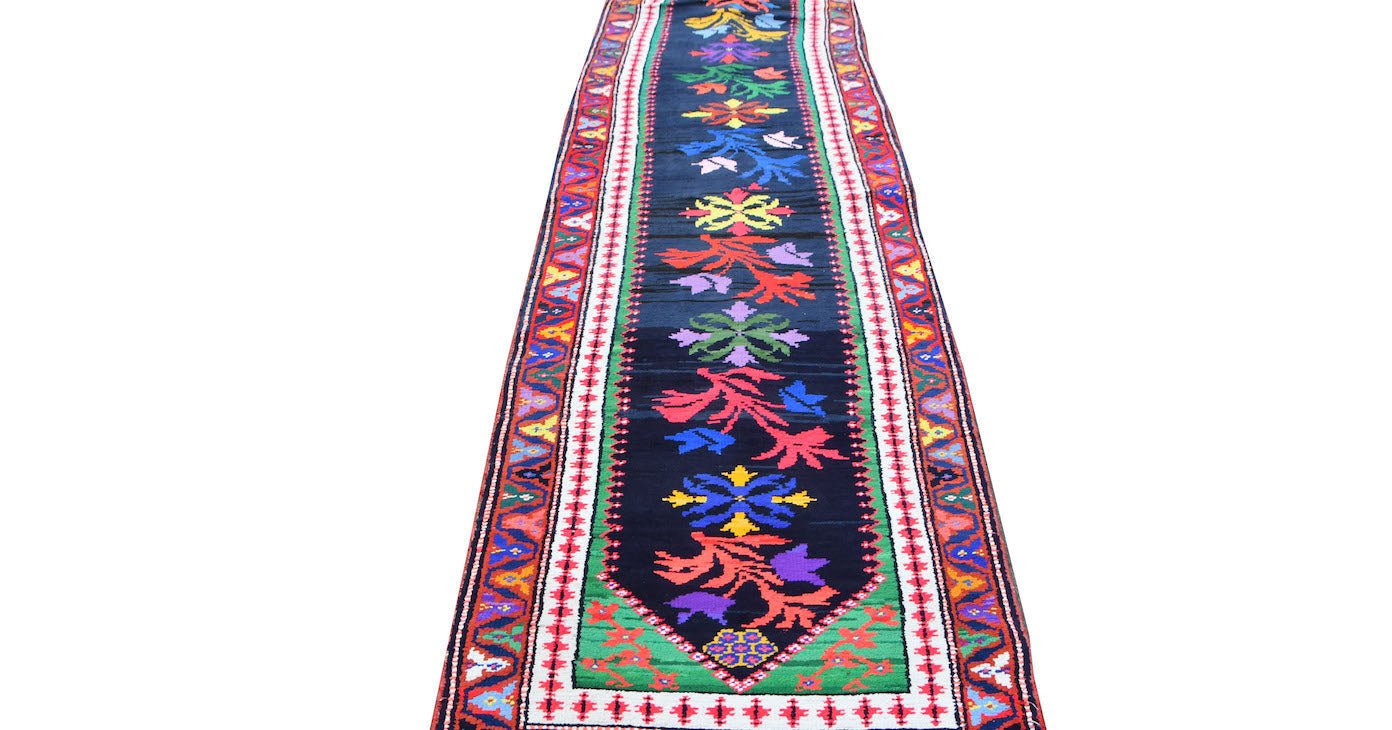 A vintage Kurdish Herki runner featuring a dark field with colorful tribal floral motifs.