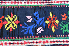 A vintage Kurdish Herki runner featuring vibrant tribal floral motifs on a dark blue wool base.