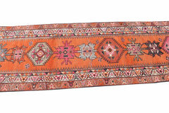 A vintage Kurdish Herki runner featuring tribal geometric motifs in vibrant orange and neon tones.