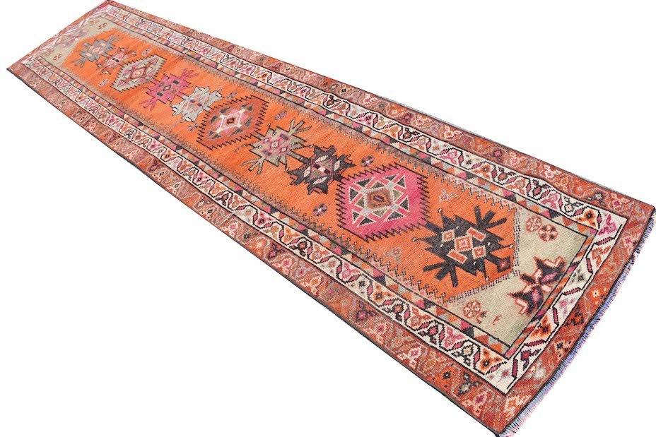 A vintage Kurdish Herki runner featuring tribal geometric motifs in vibrant orange and pink tones.