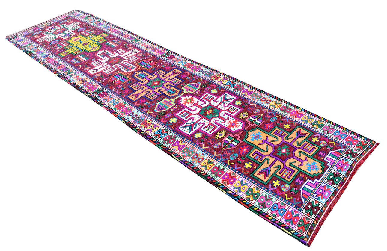 A vintage Kurdish Herki runner featuring vibrant tribal motifs in wool and nylon on a red base.