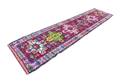 A vintage Kurdish Herki runner featuring vibrant tribal motifs on a deep red wool base.