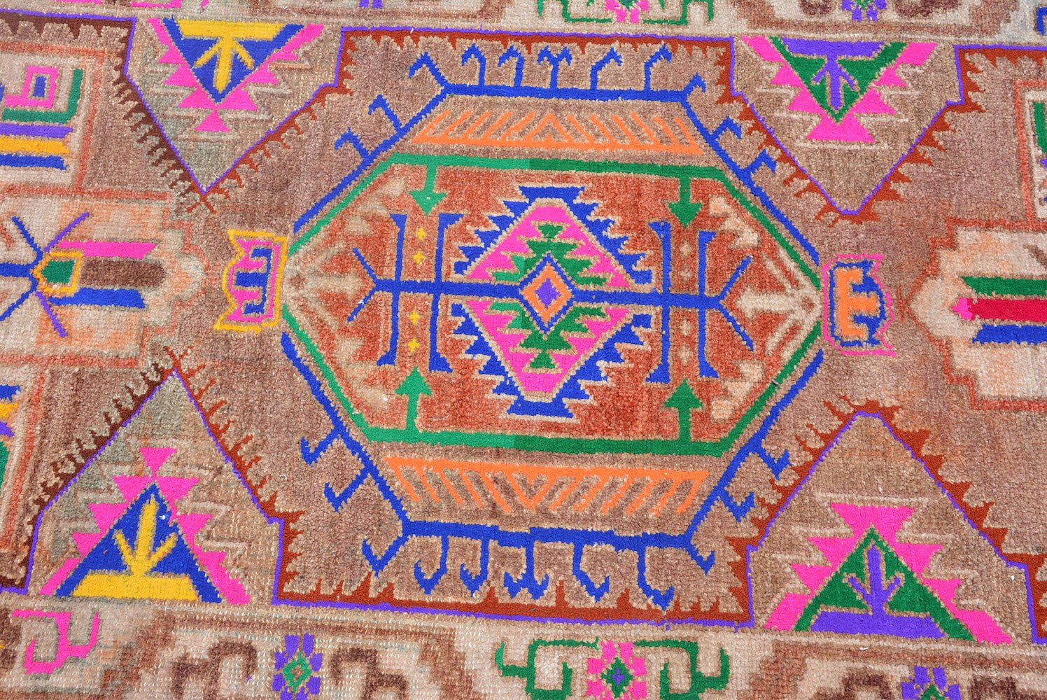 A vintage Kurdish Herki runner featuring tribal motifs in vibrant neon colors on a brown wool base.