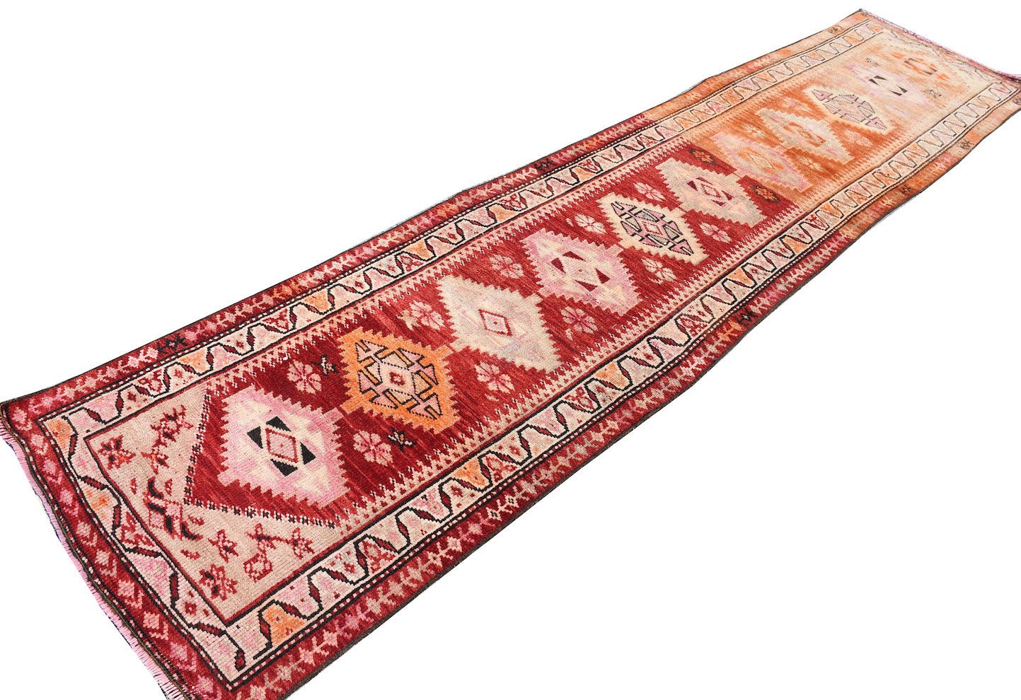 A vintage Kurdish Herki runner featuring tribal geometric motifs in red, orange, and pink tones.