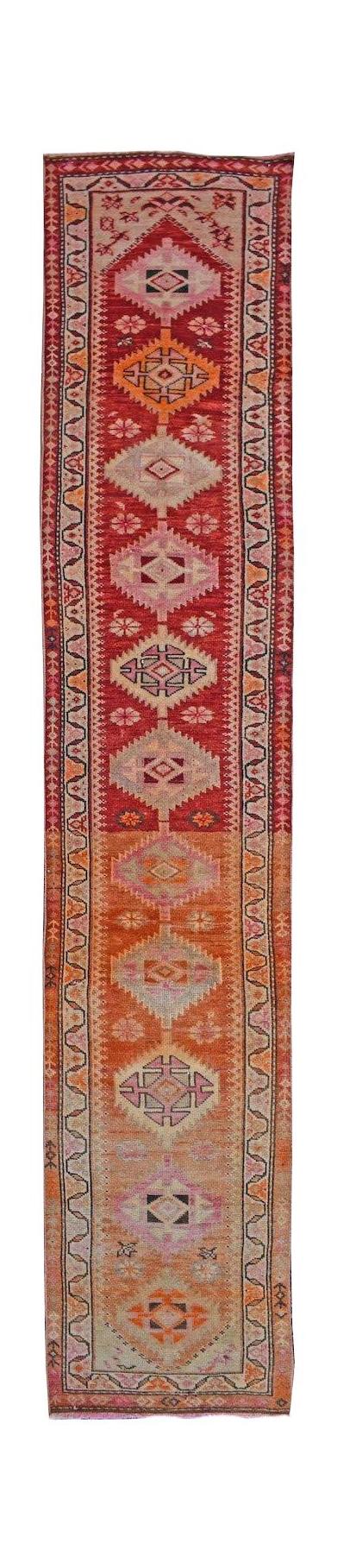 A vintage Kurdish Herki runner featuring tribal diamond motifs in vibrant red and orange tones.