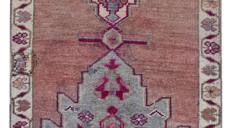 A vintage Kurdish Herki runner featuring tribal motifs in shades of pink, grey, and cream.